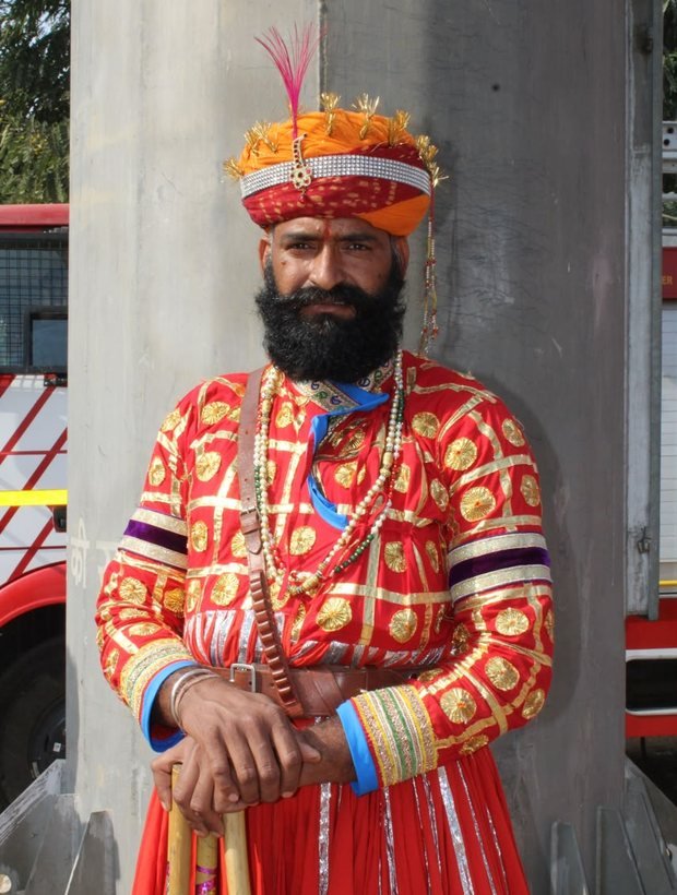 Welcome attendant in full red and gold ceremonial dress holding a staff