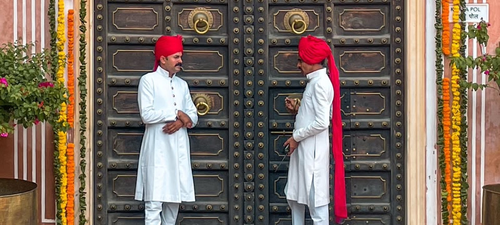 Two darban doormen in white achkans at a marigold-draped palace door in Jaipur