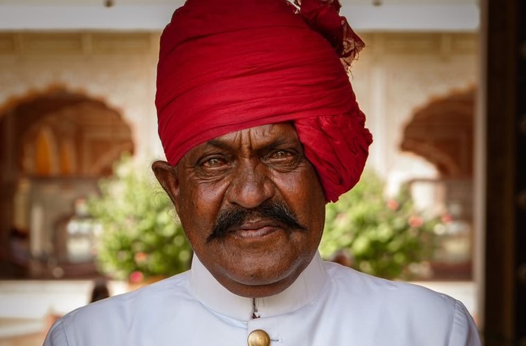 Moustached darban doorman in a red safa turban and white achkan at a palace entrance